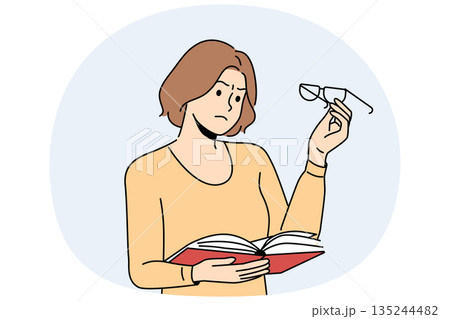 Woman experiences vision problems reading book and looks at glasses with upset grimace 135244482