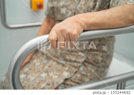 Asian elderly woman patient use toilet support rail in bathroom. 135244692