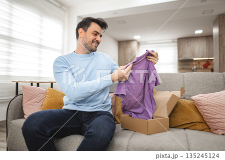Man opens the cardboard package and looks at the new T-shirt Man opens the cardboard package and looks at the new T-shirt 135245124