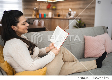 Woman reading a book while relaxing on a sofa at home 135245169