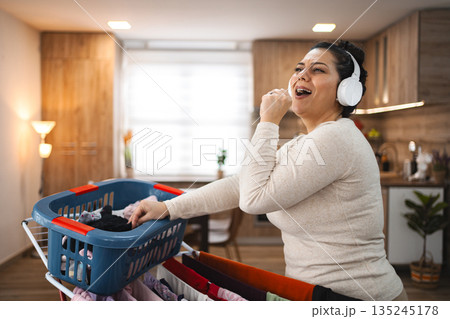 Woman singing while hanging the laundry on drying rack at home 135245178