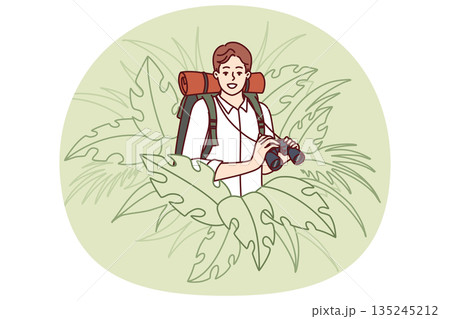 Man traveler stands in thickets of jungle and holds binoculars exploring area in search further path 135245212
