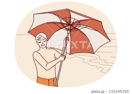 Elderly man stands on beach and holds umbrella to protect from sun during trip to tropical resort Elderly man stands on beach and holds umbrella to protect from sun during trip to tropical resort 135245250