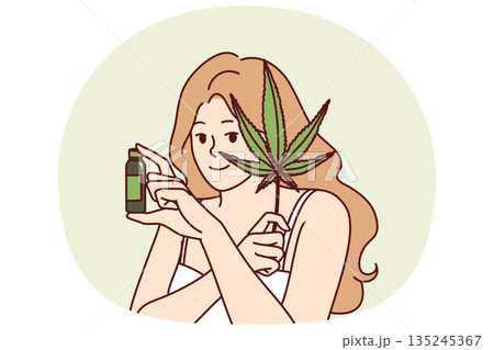 Woman uses hemp oil for skin care and fighting acne or wrinkles on face and holds marijuana leaf 135245367