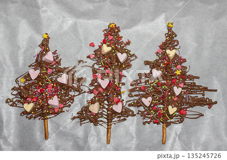 Three chocolate Christmas trees decorated with hearts sprinkles and colorful candy toppings Three chocolate Christmas trees decorated with hearts sprinkles and colorful candy toppings 135245726