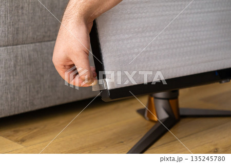 Close-up of a man's hand carefully peeling a clear protective film from the screen of a new high-performance gaming monitor during unboxing 135245780