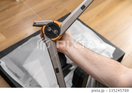 A person's hand holding a professional gray and orange tripod, highlighting its sturdy design and intricate joint for camera setup and content creation A person's hand holding a professional gray and orange tripod, highlighting its sturdy design and intricate joint for camera setup and content creation 135245789