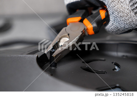 Mechanic's gloved hand expertly uses multi-functional pliers to secure a small hexagonal bolt, showcasing precision engineering and professional technical equipment assembly 135245818