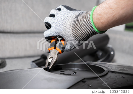 Close-up of a worker's hand in a protective glove using pliers, meticulously assembling a complex electronic device, highlighting precision work and technological repair Close-up of a worker's hand in a protective glove using pliers, meticulously assembling a complex electronic device, highlighting precision work and technological repair 135245823