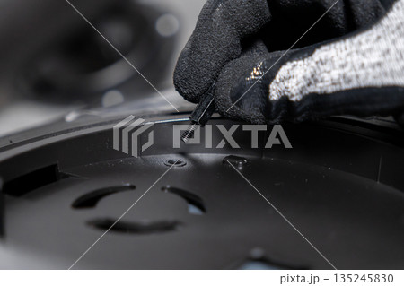 Professional's gloved hand carefully positions a tiny threaded metal standoff screw, precisely aligning it into a black electronic device, illustrating detailed assembly and repair work Professional's gloved hand carefully positions a tiny threaded metal standoff screw, precisely aligning it into a black electronic device, illustrating detailed assembly and repair work 135245830