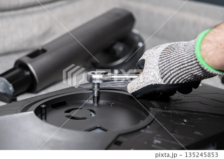 Gloved hand uses ratchet wrench to secure component on electronic device, illustrating detailed assembly, technical repair, and maintenance 135245853