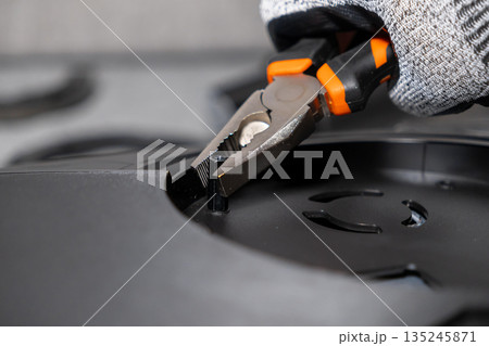 Expert hand in work glove uses orange pliers to install a small black hex standoff, symbolizing meticulous electronic assembly and technical repair Expert hand in work glove uses orange pliers to install a small black hex standoff, symbolizing meticulous electronic assembly and technical repair 135245871
