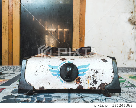 Rusty Single Burner Gas Stove on a Patterned Tabletop in a Rustic Kitchen. 135246363