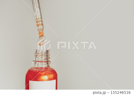 Cosmetic serum dropper above glass bottle with shimmering liquid Cosmetic serum dropper above glass bottle with shimmering liquid 135246516