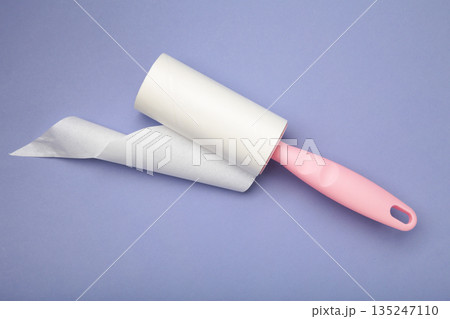 Cloth fabrics cleaner lint roller brush with paper roll on purple background. Sticky roller, pet cat dog fur dust hair remover Cloth fabrics cleaner lint roller brush with paper roll on purple background. Sticky roller, pet cat dog fur dust hair remover 135247110