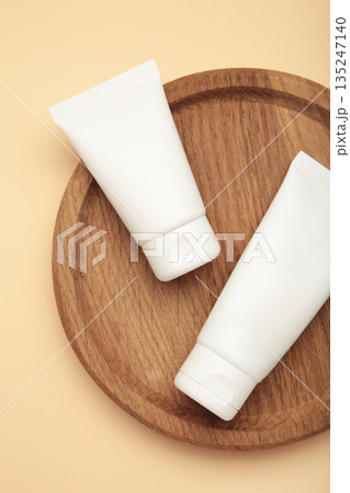 White cosmetics tube with cotton flowers on wooden plate on beige background. Vertical photo White cosmetics tube with cotton flowers on wooden plate on beige background. Vertical photo 135247140