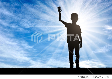 A silhouette of a disabled boy with a prosthetic arm, highlighted by the sun shining in the background 135247280