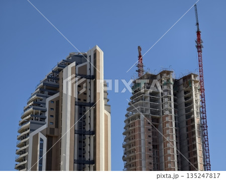 highrise juxtaposition with twin cranes, cityscape showing retrofit options and contrasting facades 135247817