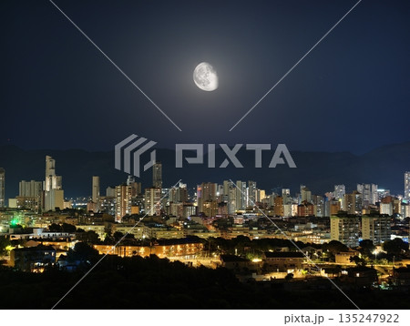 City skyline illuminated by moon and reflecting in calm waters 135247922
