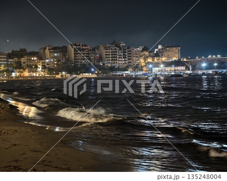 Dusk scenery with shimmering city lights and tranquil surf 135248004