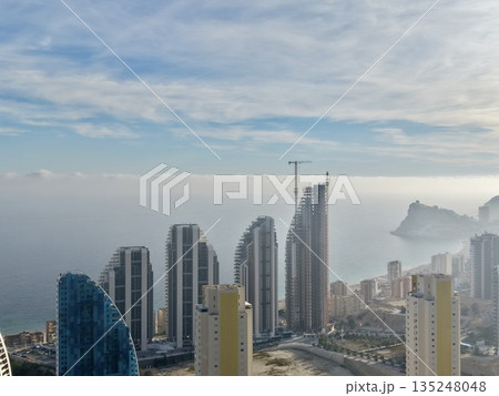 calm coastal skyscraper ensemble with haze, gentle fog over tranquil sea and rocky formations calm coastal skyscraper ensemble with haze, gentle fog over tranquil sea and rocky formations 135248048