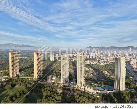 urban area meets mountain range, city sprawls towards towering mountains beneath clear bright sky 135248053