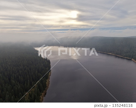 serene landscape featuring still pond enclosed by vibrant evergreen forests and shimmering surfaces 135248118