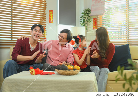 Asian family relaxing together on sofa, watching television after a Chinese New Year meal 135248986