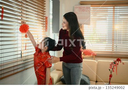 Mother and daughter decorate a home with lanterns on window with his mother for Lunar New Year celebration. 135249002