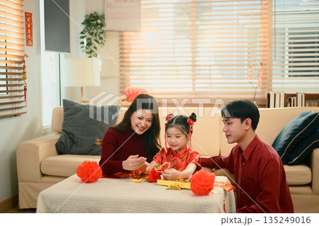 Asian family sit together decorating red lanterns ornaments for Chinese New Year, sharing a joyful family moment 135249016