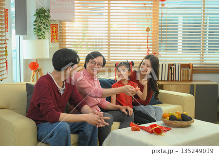 Asian family relaxing together on sofa, watching television after a Chinese New Year meal 135249019