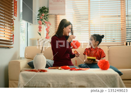 Mother and daughter sit together decorating red lanterns ornaments for Chinese New Year, sharing a joyful family moment Mother and daughter sit together decorating red lanterns ornaments for Chinese New Year, sharing a joyful family moment 135249023