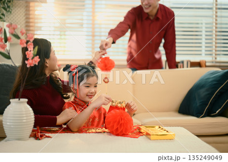 Happy family decorating home for Chinese New Year as father hands a red ornament to mother and daughter 135249049
