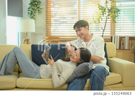 Young couple relaxing on sofa, shopping online together with a tablet on Valentine Day, enjoying love, comfort Young couple relaxing on sofa, shopping online together with a tablet on Valentine Day, enjoying love, comfort 135249063