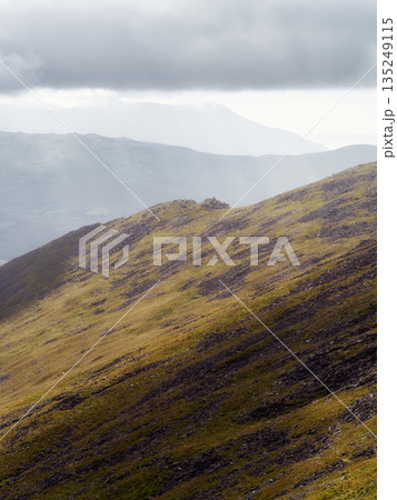 Sunlit mountain ridge with a grassy slope leads against a bright backdrop. Sunlit mountain ridge with a grassy slope leads against a bright backdrop. 135249115