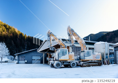 Scenic view frozen hydraulic excavators standing outdoors winter conditions covered snow ice industrial building alpine area. Cold weather impacts machinery operation hydraulic systems reliability Scenic view frozen hydraulic excavators standing outdoors winter conditions covered snow ice industrial building alpine area. Cold weather impacts machinery operation hydraulic systems reliability 135249219