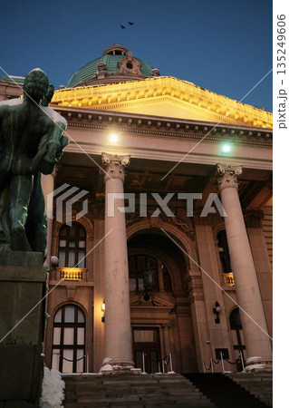 Monument stands before an illuminated historic building during winter evening. The scene represents cultural heritage, urban identity, and seasonal city atmosphere 135249606