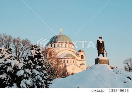 Orthodox St Sava church in Belgrade and historic monument stand covered with snow under clear winter sky. The scene reflects cultural heritage, faith, and winter atmosphere in the city 135249638
