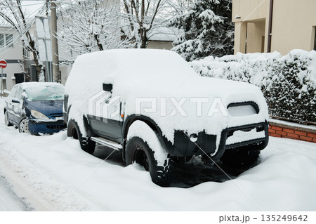 SUV stands parked on a city street completely covered with heavy snow. The image represents extreme winter weather and its effect on urban transportation SUV stands parked on a city street completely covered with heavy snow. The image represents extreme winter weather and its effect on urban transportation 135249642