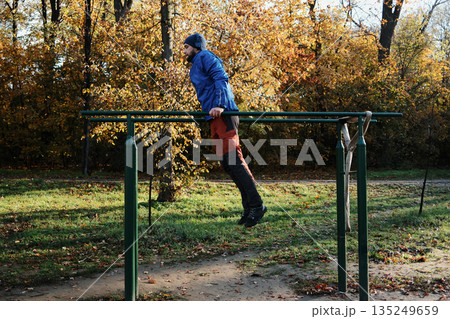 A man exercises on parallel bars in a park. The moment reflects discipline and committed outdoor training A man exercises on parallel bars in a park. The moment reflects discipline and committed outdoor training 135249659
