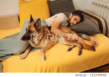 A man sleeps on a bed holding a German Shepherd, showing morning rest and human pet bonding A man sleeps on a bed holding a German Shepherd, showing morning rest and human pet bonding 135249690