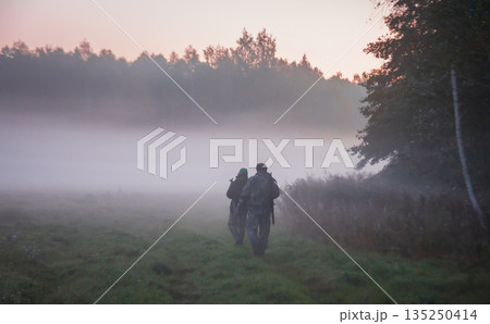 Hunter and huntsman walk cautiously in fog along edge of forest. Hunter and huntsman walk cautiously in fog along edge of forest. 135250414