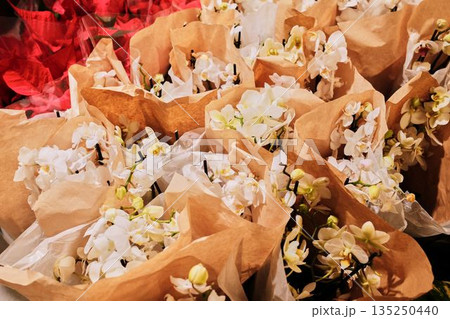 Elegant white orchids wrapped in brown paper ready for sale in a flower shop. The concept represents purity, simplicity, and refined natural beauty 135250440
