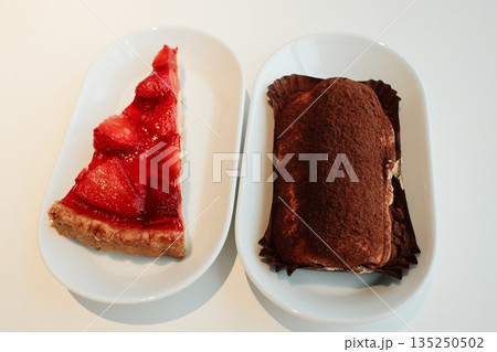 Two elegant desserts, one strawberry tart and one tiramisu, displayed side by side on white plates in bright natural light Two elegant desserts, one strawberry tart and one tiramisu, displayed side by side on white plates in bright natural light 135250502