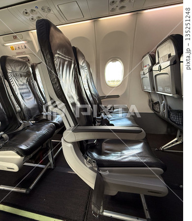 Airplane interior with black leather seats arranged near exit row and window section. Travel, mobility, and modern aviation comfort highlighting passenger transport and tourism lifestyle. Airplane interior with black leather seats arranged near exit row and window section. Travel, mobility, and modern aviation comfort highlighting passenger transport and tourism lifestyle. 135251248