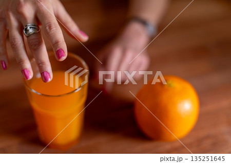 Closeup of hand near juice glass, Casual domestic moment with beverage on kitchen counter, Photographic portrayal of personal moment involving glass of juice and details 135251645