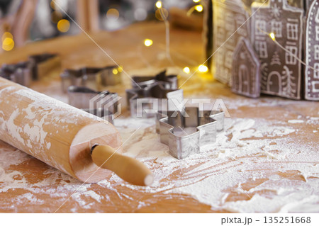 Baking gingerbread cookie cutters, wooden rolling pin, and flour are messily spread on kitchen table Baking gingerbread cookie cutters, wooden rolling pin, and flour are messily spread on kitchen table 135251668