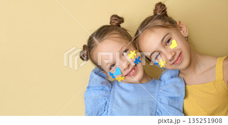 Positive children with pieces of yellow and blue puzzles and hearts on cheeks. A symbol in support of people with down syndrome. Positive children with pieces of yellow and blue puzzles and hearts on cheeks. A symbol in support of people with down syndrome. 135251908
