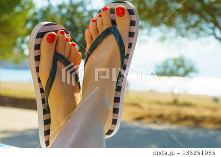 Female feet wearing flip flops having red nails 135251985