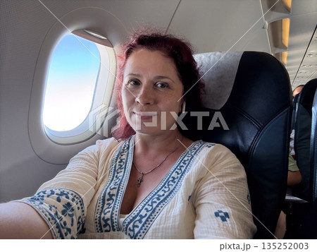 Passenger woman looking through airplane window during flight. Travel, contemplation, and personal experience of air journey. 135252003